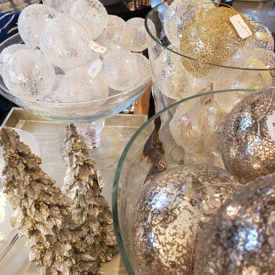 Frosted and gilded glass baubles in footed bowls beside glittered trees.