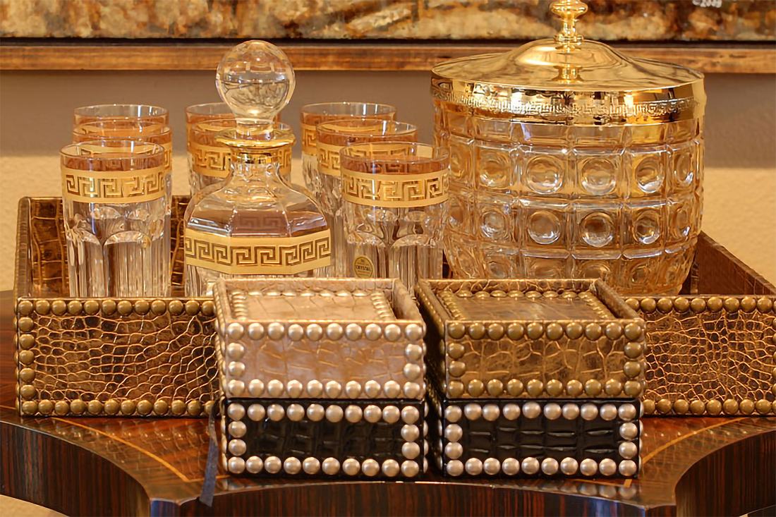 Gilt-banded crystal barware and studded leather boxes on a tray.