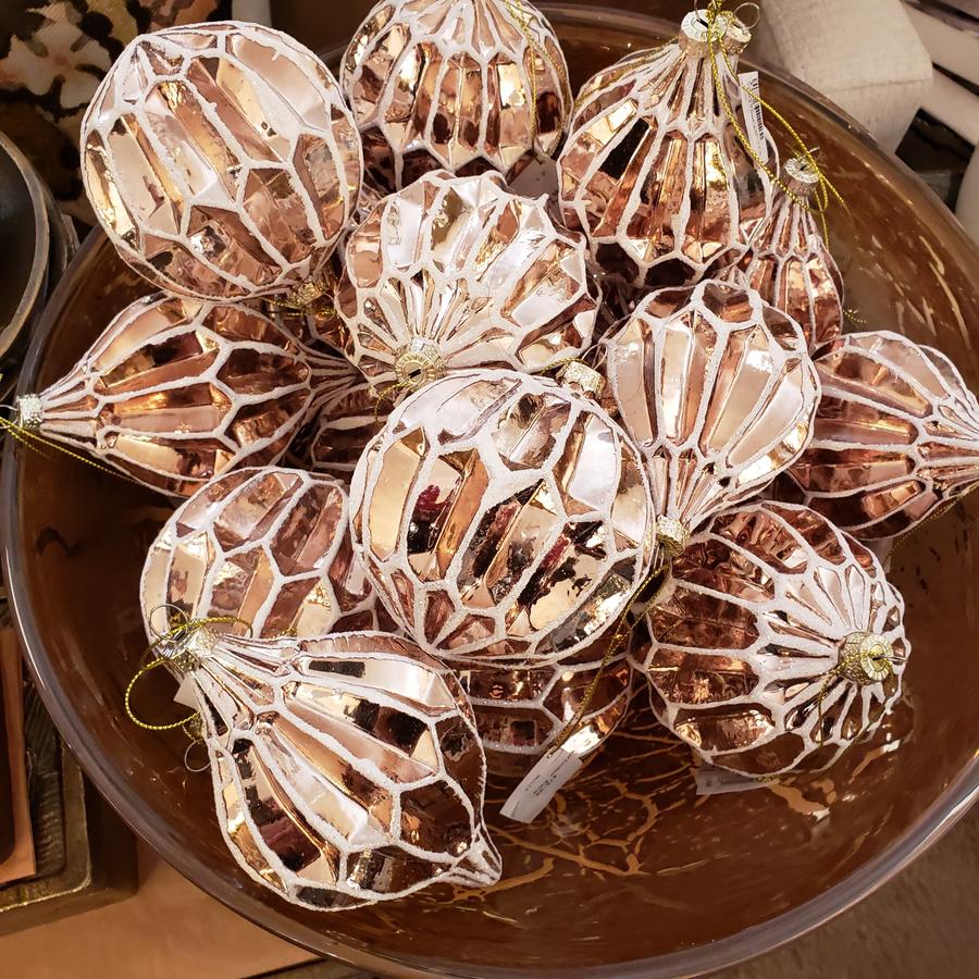 A bowl of rose gold mercury glass ornaments with frosted white detailing.